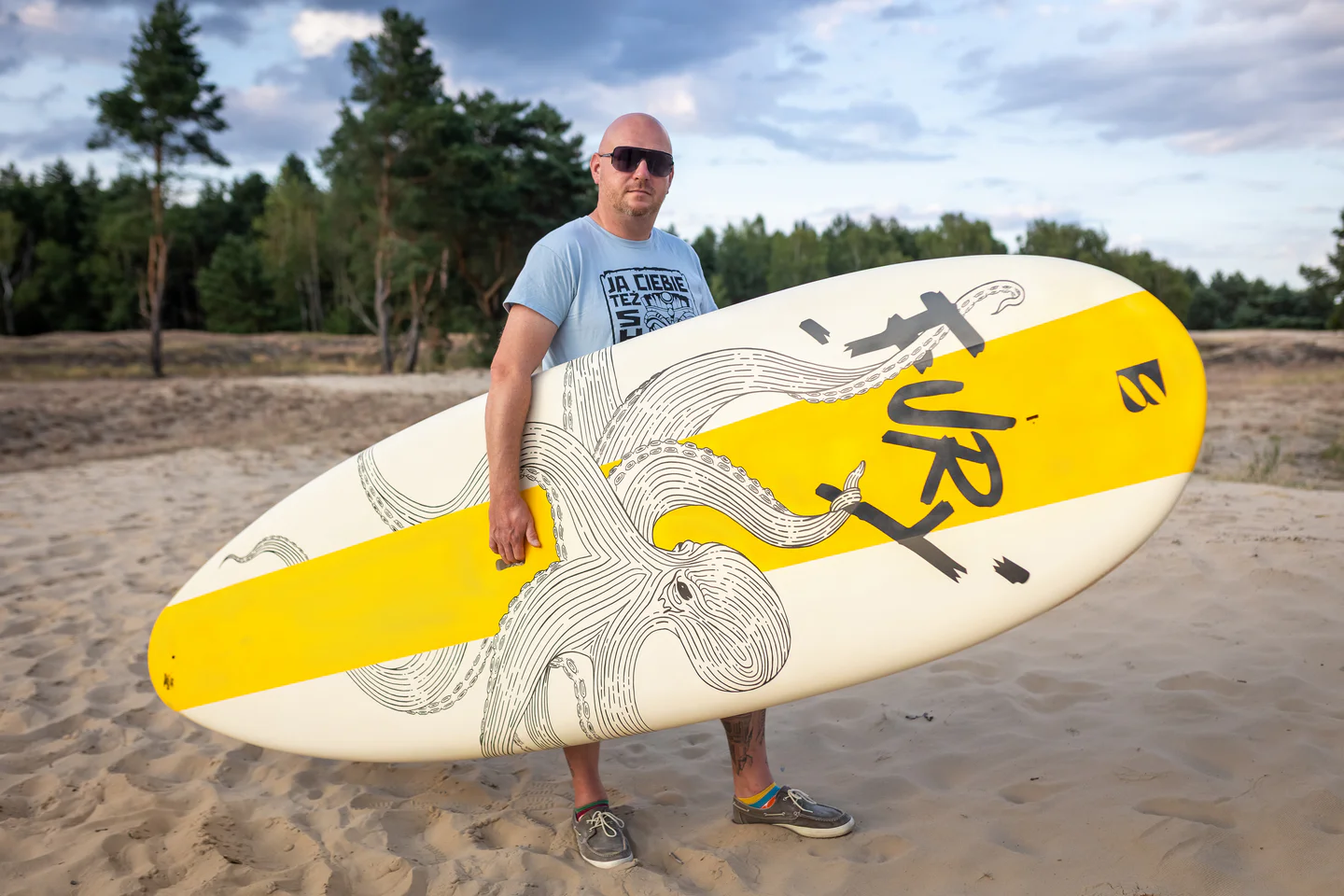 Mezczyzna trzymajacy deske sztywna do surfingu marki Bass Polska.webp