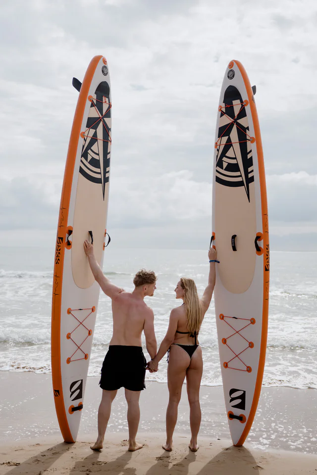 Para stojąca na plaży z deskami SUP Bass Morning Star trzymanymi w pionie
