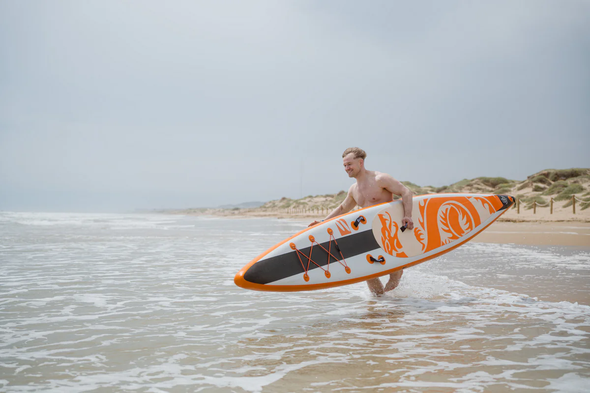 Bass SUP Dragon 14.6 – młody mężczyzna z deską SUP na plaży w słonecznej Hiszpanii