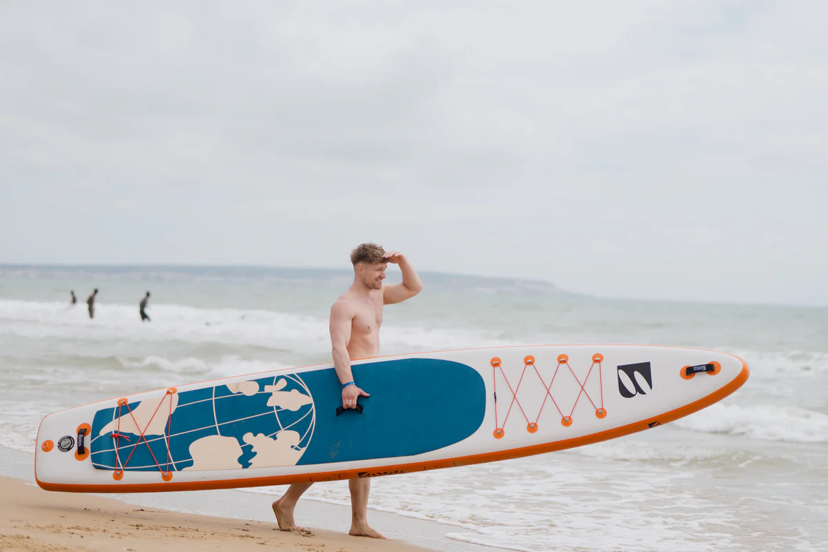 Bass SUP Explorer 14 – młody mężczyzna z deską SUP na słonecznej plaży w Hiszpanii