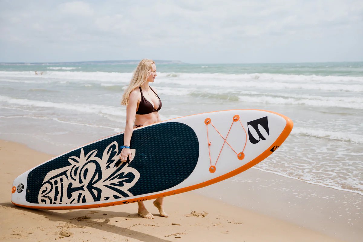 Bass SUP Wind and Wing 10 – młoda kobieta z deską SUP na słonecznej plaży w Hiszpanii