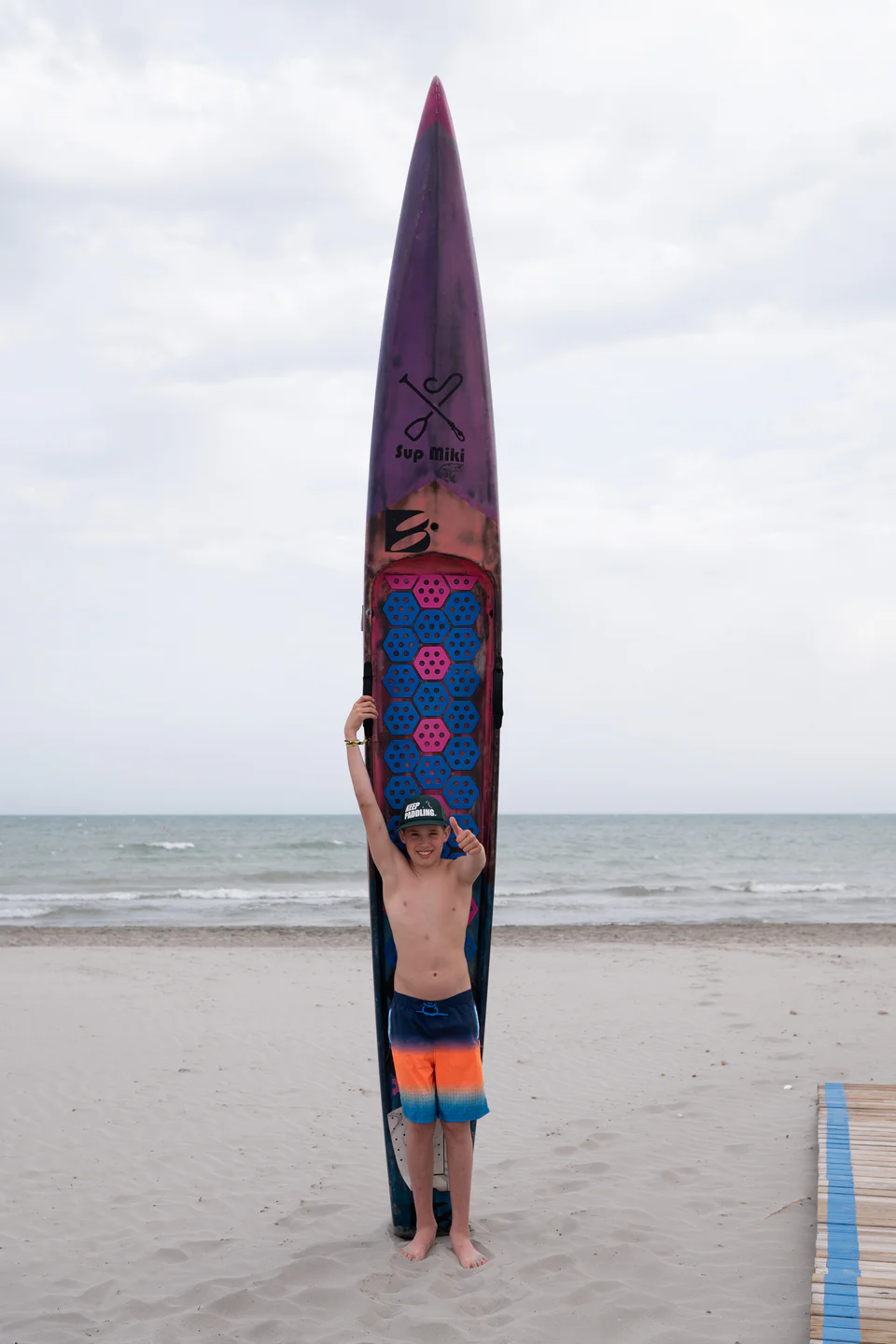 Chłopak stoi na plaży z purpurową sztywną deską SUP z karbonu marki Bass Polska